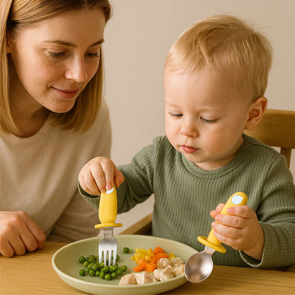 Bébé assis à table mange avec la cuillère CuttieSpoon™ en silicone alimentaire, sous le regard bienveillant de sa maman — apprentissage de l’autonomie et repas en toute sécurité.